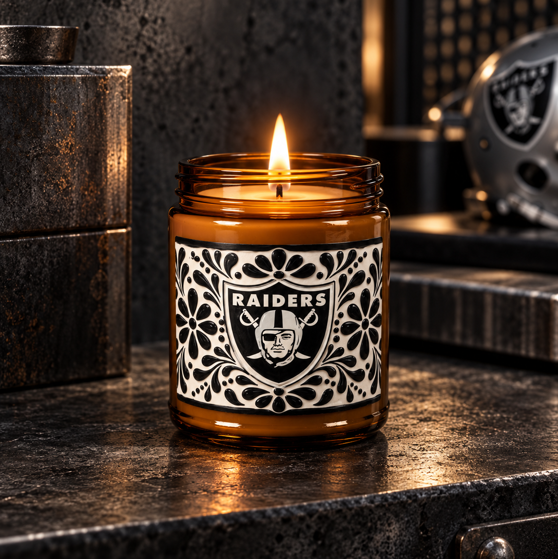 A lit amber glass jar candle with a black-and-white Raiders logo label, set on a dark metallic surface in a moody, industrial-style setting.