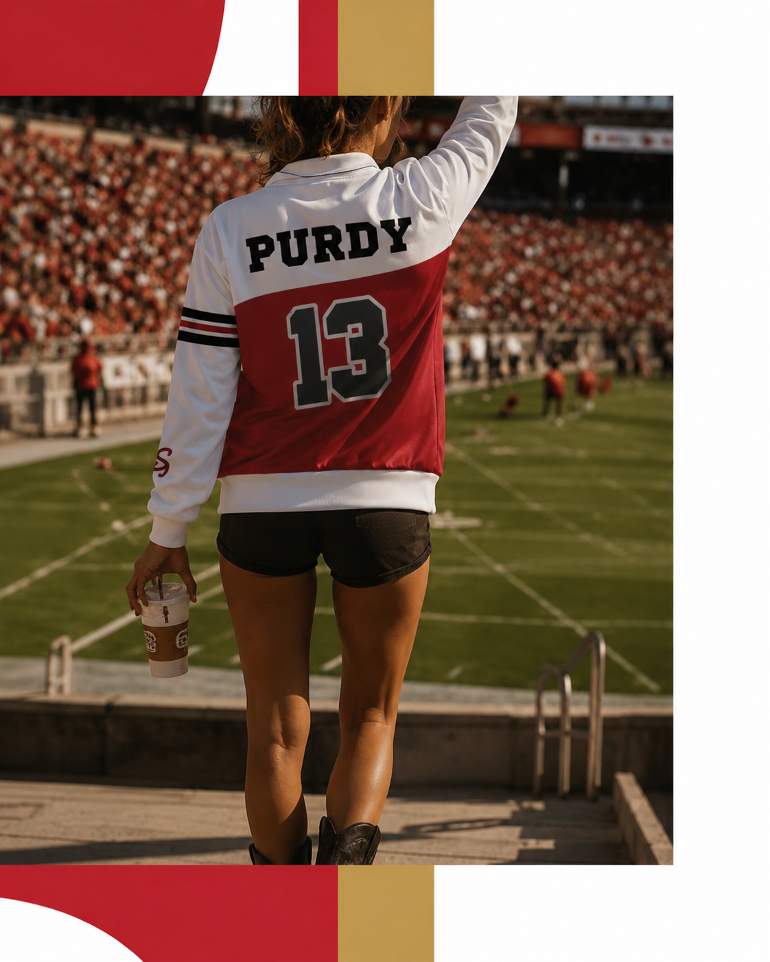 A person seen from behind wearing a red and white long-sleeve sports jersey with 'PURDY 13' on the back, standing on a stadium walkway with a field and crowd in the background.
