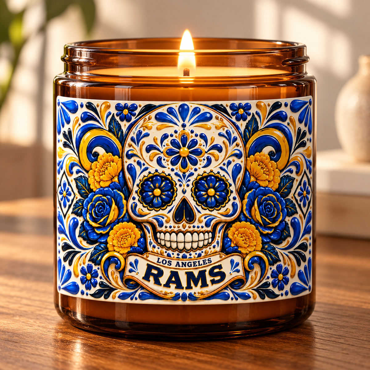 An amber glass jar candle with a lit flame, featuring a colorful Day of the Dead sugar skull label with blue, yellow, and white floral details and the text 'Los Angeles Rams'.