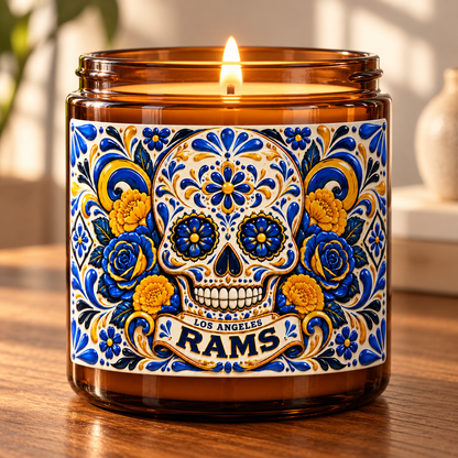 An amber glass jar candle with a lit flame, featuring a colorful Day of the Dead sugar skull label with blue, yellow, and white floral details and the text 'Los Angeles Rams'.