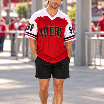 A man wearing a red and white San Francisco 49ers athletic jersey with black shorts and red/black sneakers, standing outdoors in a stadium-like environment.